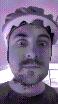a selfie of a white person, wearing either headphones or a helmet, making an odd expression. the photo is edited to be colorized into a monochrome purple-ish color palette.